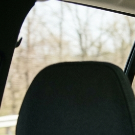 Tres niños viajando en la parte trasera del auto, dos en sillas infantiles y uno con cinturón, ilustrando distribución segura de asientos para niños.