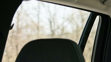 Tres niños viajando en la parte trasera del auto, dos en sillas infantiles y uno con cinturón, ilustrando distribución segura de asientos para niños.