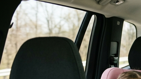 Tres niños viajando en la parte trasera del auto, dos en sillas infantiles y uno con cinturón, ilustrando distribución segura de asientos para niños.