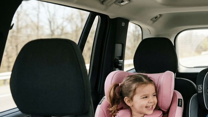 Tres niños viajando en la parte trasera del auto, dos en sillas infantiles y uno con cinturón, ilustrando distribución segura de asientos para niños.