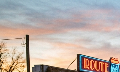 Tres autos clásicos (un Pontiac, un Oldsmobile y un Plymouth) estacionados frente a un restaurante retro de la Ruta 66 durante el atardecer.