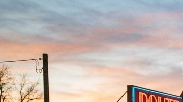 Tres autos clásicos (un Pontiac, un Oldsmobile y un Plymouth) estacionados frente a un restaurante retro de la Ruta 66 durante el atardecer.