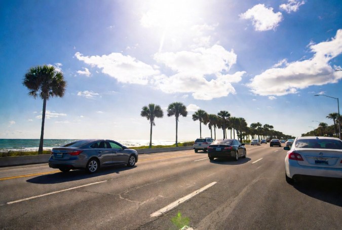 Carretera costera de Florida con autos circulando bajo un cielo soleado junto al mar y palmeras.