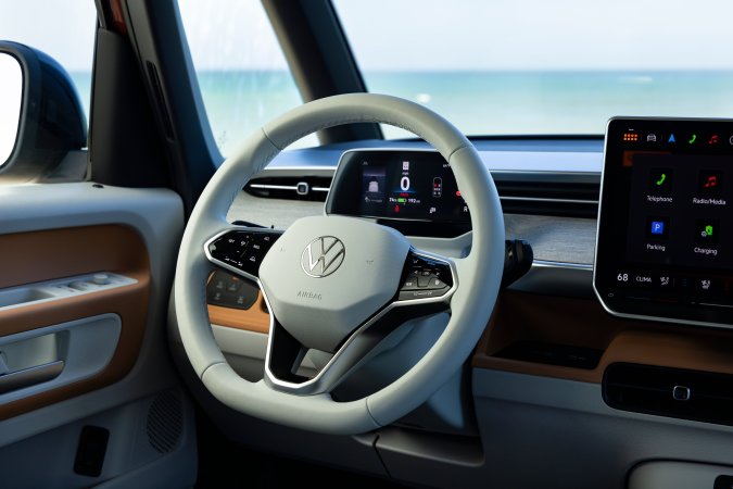 Interior del Volkswagen ID. Buzz con volante multifunción y pantalla digital, vista panorámica al mar. Diseño moderno y minimalista.