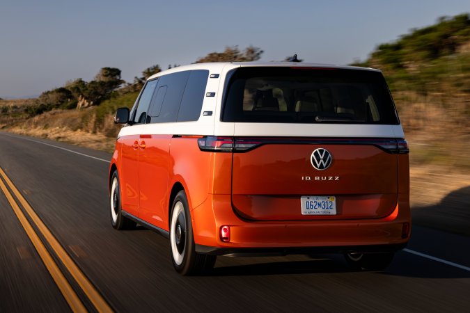 Volkswagen ID. Buzz naranja circulando en carretera costera. Vista trasera 3/4 del icónico van eléctrico de Volkswagen.