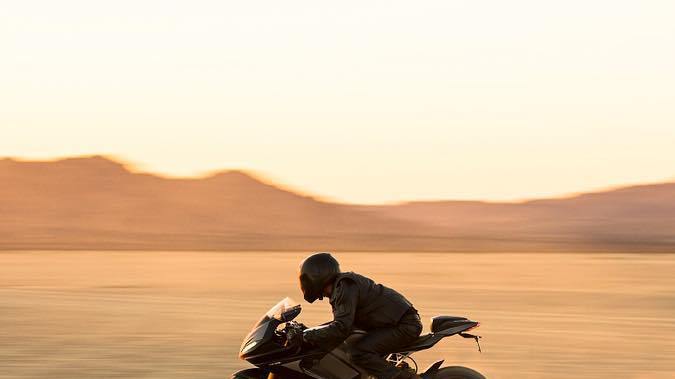 Lightning LS-218, moto eléctrica superdeportiva, circulando a alta velocidad sobre desierto al atardecer.