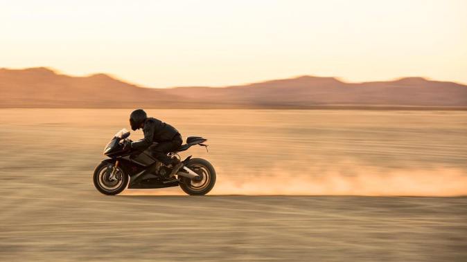 Lightning LS-218, moto eléctrica superdeportiva, circulando a alta velocidad sobre desierto al atardecer.
