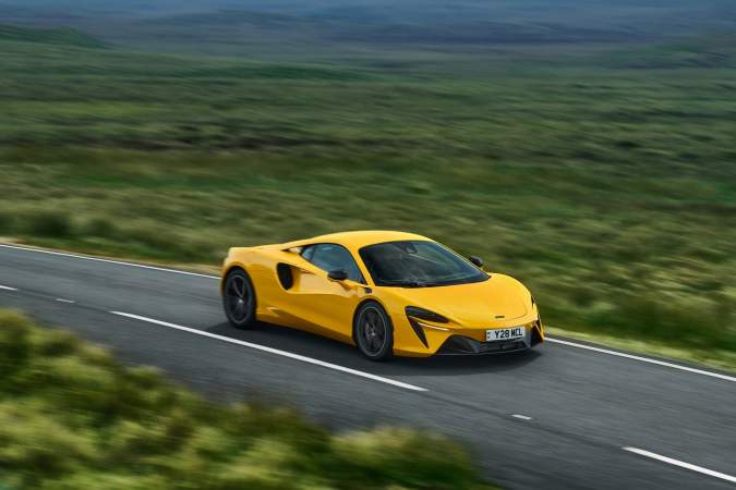 McLaren Artura amarillo circulando por carretera abierta, superdeportivo híbrido enchufable demostrando alto rendimiento y eficiencia en entorno rural