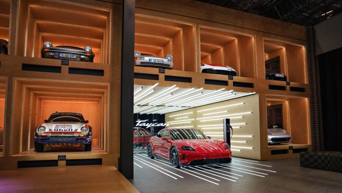 Exposición de Porsche Taycan GTS rojo en showroom moderno, rodeado de clásicos Porsche, resaltando evolución de deportivos eléctricos de alto rendimiento