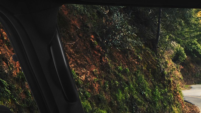 Interior del Lexus GX 2026 con pantalla táctil grande, tablero digital y vista panorámica de carretera sinuosa entre árboles desde el asiento del conductor.