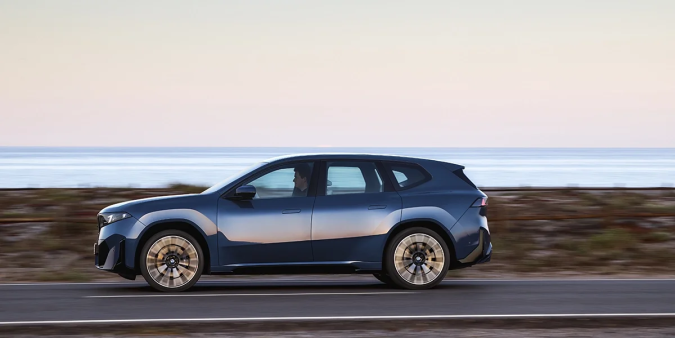 BMW iX3 50 azul circulando junto al mar, elegante diseño exterior del SUV eléctrico premium de BMW.