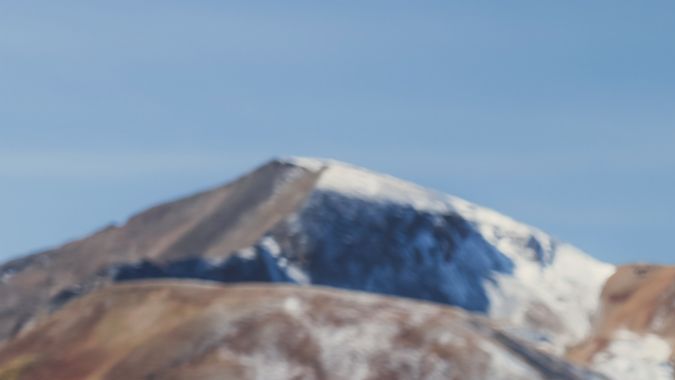 Porsche Macan Eléctrico azul en montaña, detalle lateral con llanta Michelin y paisaje nevado de fondo.