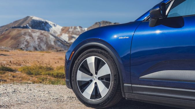 Porsche Macan Eléctrico azul en montaña, detalle lateral con llanta Michelin y paisaje nevado de fondo.