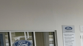 Fotografía de plano medio que muestra el interior de un concurrido taller de servicio de concesionario Ford, capturando la actividad de los técnicos trabajando en varios vehículos de la marca, como el Mustang Mach-E y el Ford Bronco Sport