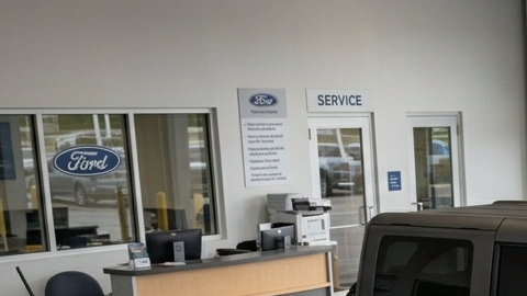 Fotografía de plano medio que muestra el interior de un concurrido taller de servicio de concesionario Ford, capturando la actividad de los técnicos trabajando en varios vehículos de la marca, como el Mustang Mach-E y el Ford Bronco Sport