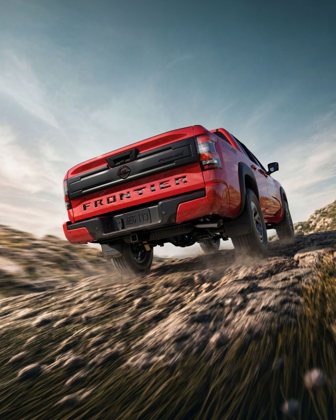 Nissan Frontier PRO-4X roja 2026 en acción off-road, vista trasera dinámica sobre terreno irregular.