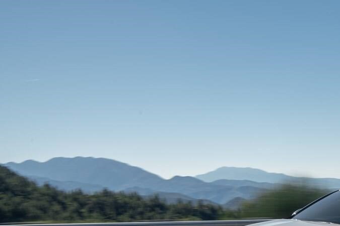 Kia K5 2026 plateado en movimiento en autopista. Sedán elegante con diseño deportivo y paisaje montañoso