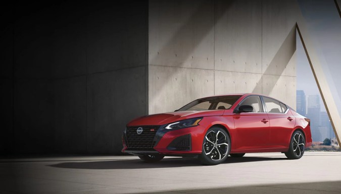 Nissan Altima SR 2026 roja con estilo agresivo. Sedán deportivo estacionado con fondo urbano y arquitectura moderna