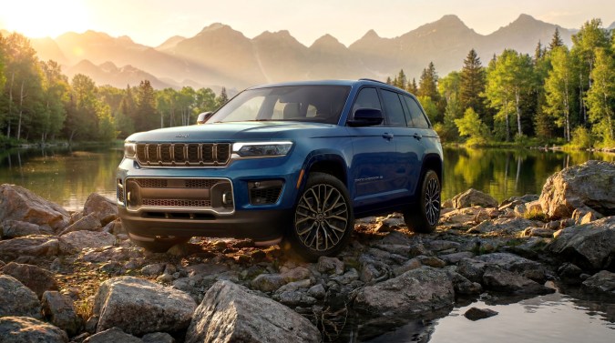 Jeep Grand Cherokee Overland 2027 azul, SUV frente a lago y montañas, diseño robusto y elegante, ideal para aventuras todoterreno y familia.