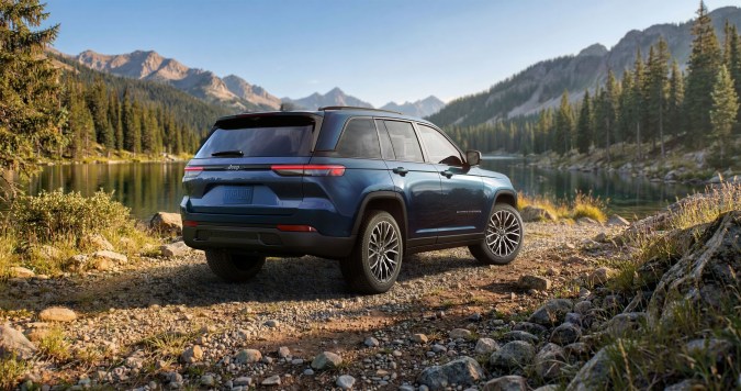 Jeep Grand Cherokee Overland 2027 azul visto desde atrás, junto a lago de montaña, llantas grandes y diseño elegante, SUV ideal para rutas panorámicas largas.