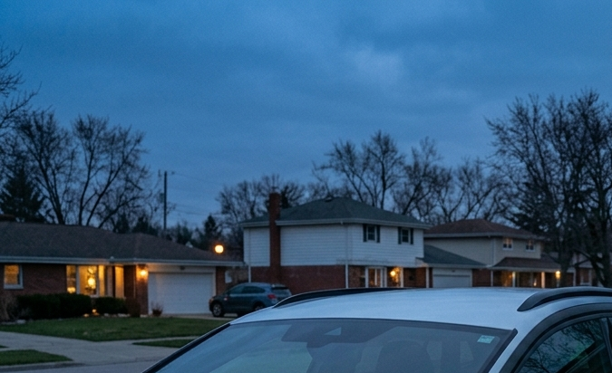 Propietario conectando Volkswagen ID eléctrico blanco a cargador doméstico en casa suburbana al atardecer con panel solar