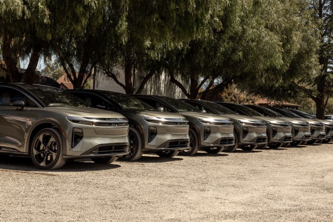 Fila de SUVs Lucid eléctricos estacionados en hilera bajo árboles, vehículos premium de lujo en exterior.