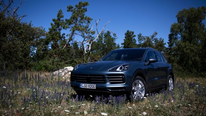 Porsche Cayenne azul en campo de flores silvestres bajo cielo azul, paisaje natural en Sueci