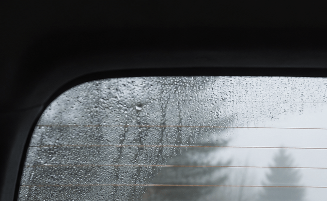 Vidrio trasero empañado con gotas de lluvia en auto. Vista de carretera con niebla a través del parabrisas posterior.
