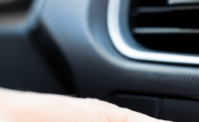 Mano presionando botón del desempañador trasero en tablero de auto. Interruptor antiempañante activado con luz indicadora