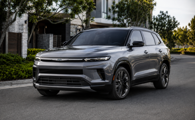 Nuevo Chrysler SUV eléctrico gris con líneas premium, estacionado en entorno residencial de lujo.