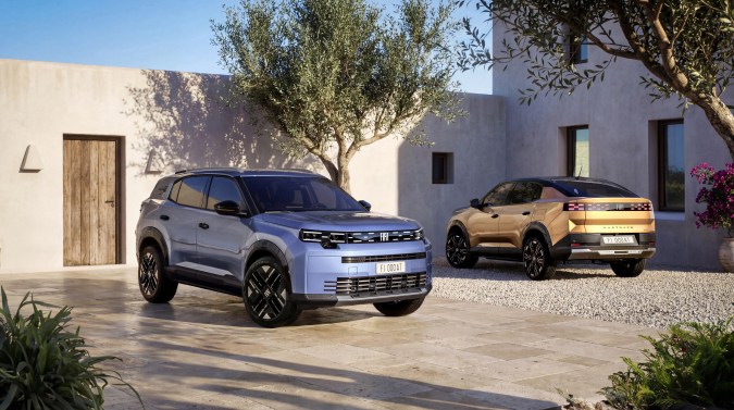 Fiat SUV azul y Fiat Fastback dorado en patio mediterráneo, vehículos eléctricos con diseño italiano moderno.