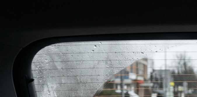 Líneas desempañadoras del vidrio trasero encendidas en coche. Vista de tráfico urbano con sistema antiempañante funcionando