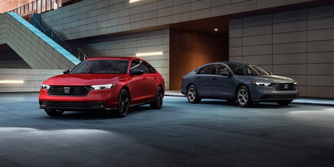 Honda Accord 2026 rojo y gris exhibidos frente a edificio moderno. Sedanes confiables y de alto diseño.