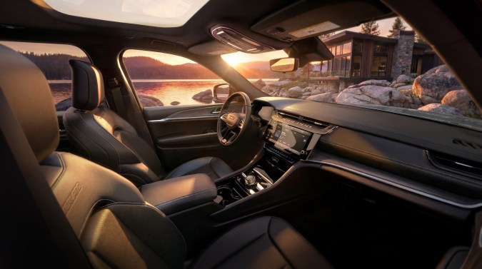 Interior del Jeep Grand Cherokee Overland 2027, asientos de cuero y tablero tecnológico, vista al lago al atardecer, SUV premium para viajes de lujo.