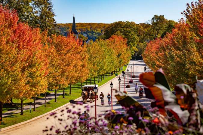 Mackinac Island en otoño, avenida arbolada con colores vibrantes, carroza de caballos y iglesia al fondo. Turismo Michigan