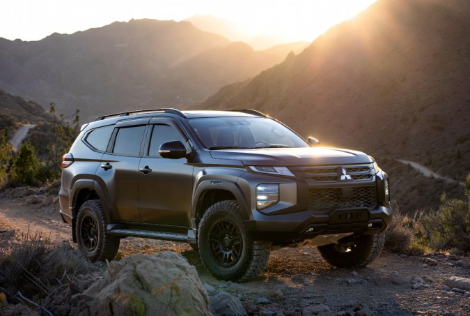Mitsubishi Montero SUV gris oscuro todoterreno en camino rocoso de montaña al atardecer, con luces LED encendidas.