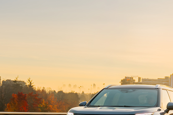 Mitsubishi Outlander Sport gris conduciendo en curva al atardecer, SUV potente con paisaje urbano y movimiento dinámico.