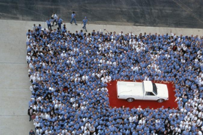 Histórica foto con trabajadores japoneses formando la bandera de Japón alrededor de una pickup Nissan Frontier blanca.