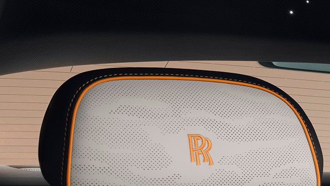 Interior trasero Rolls-Royce Spectre Series II con asientos de cuero claro, detalles naranjas y lujo artesanal en el coupé eléctrico de ultra lujo.