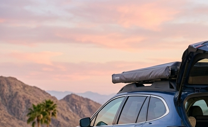 Mujer disfrutando viaje en auto con Subaru Outback equipado para acampar al atardecer en montañas. Accesorios para road trip