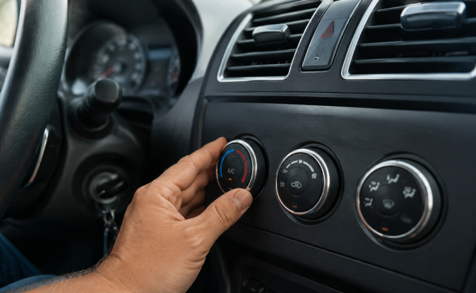 Mano girando botón de aire acondicionado A/C en el panel de climatización del vehículo, detalle del control de temperatura.
