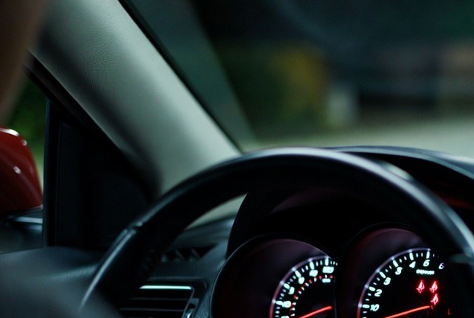 Tablero de auto con luces de alerta de cinturón de seguridad encendidas y mano en el volante.
