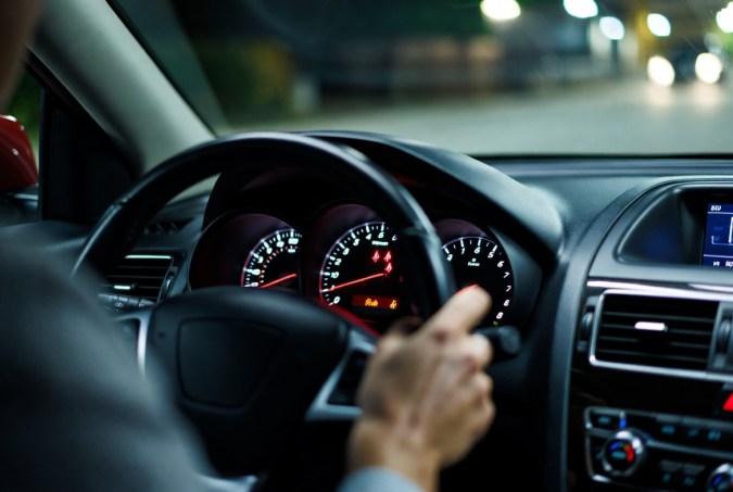 Tablero de auto con luces de alerta de cinturón de seguridad encendidas y mano en el volante.