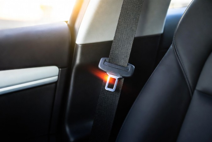 Cinturón de seguridad abrochado con luz roja de alerta iluminada en el cierre, detalle interior de vehículo.
