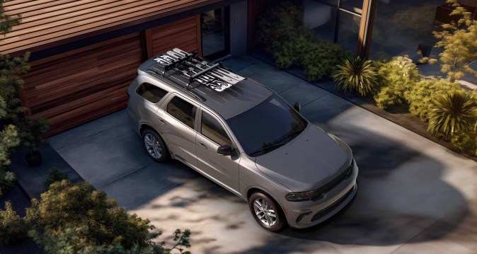 Vista aérea del Dodge Durango SRT 2026 gris con baca portaequipajes frente a casa moderna.