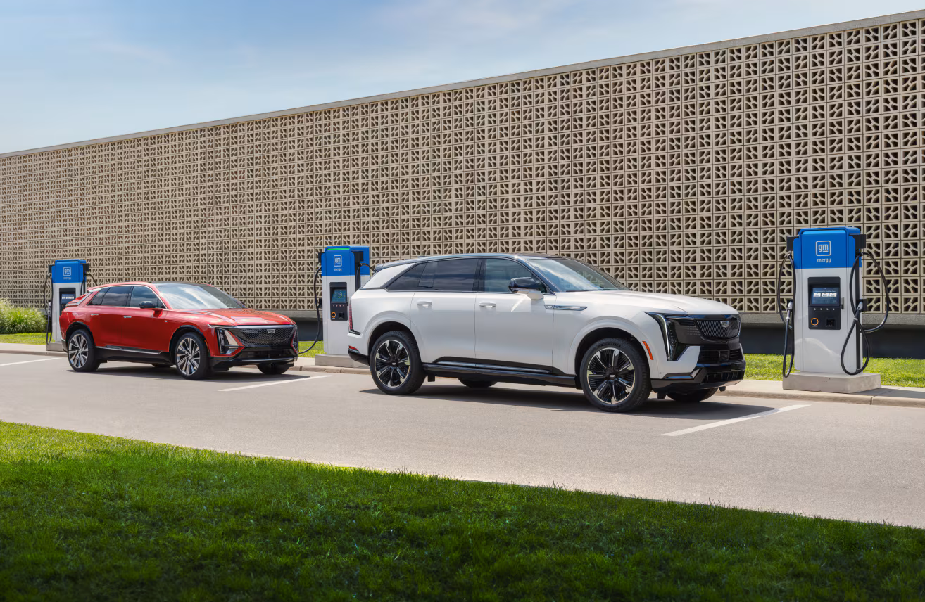 SUV eléctricos Cadillac rojo y blanco cargando en estación GM Energy al aire libre, infraestructura de carga rápida para autos eléctricos y soluciones de energía sostenible.