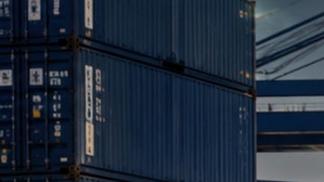 Pickup, SUV y deportivo estadounidense en puerto industrial, listos para exportación junto a contenedores y buque carguero.