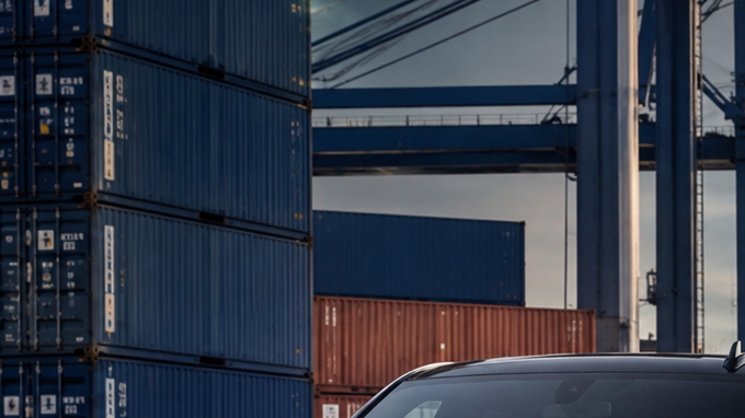 Pickup, SUV y deportivo estadounidense en puerto industrial, listos para exportación junto a contenedores y buque carguero.