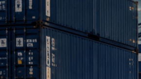 Pickup, SUV y deportivo estadounidense en puerto industrial, listos para exportación junto a contenedores y buque carguero.