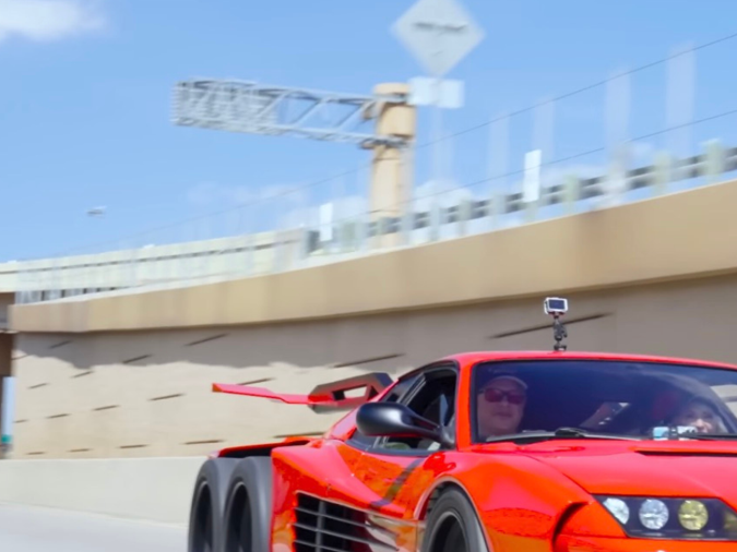 Ferrari Testarossa 6x6 naranja conduciendo a alta velocidad en autopista con efecto de movimiento